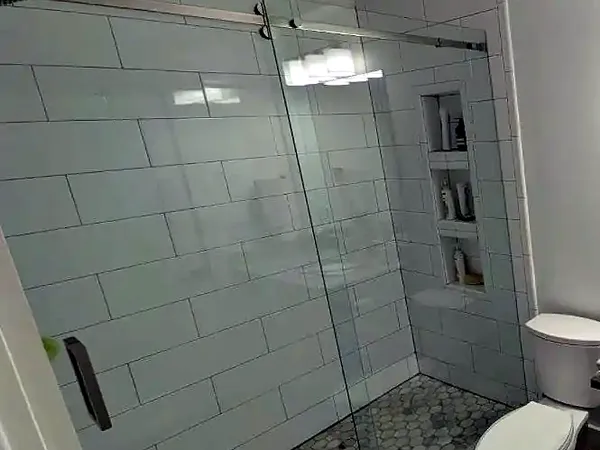 Shower with a sliding glass door, large white wall tile and a built-in niche
