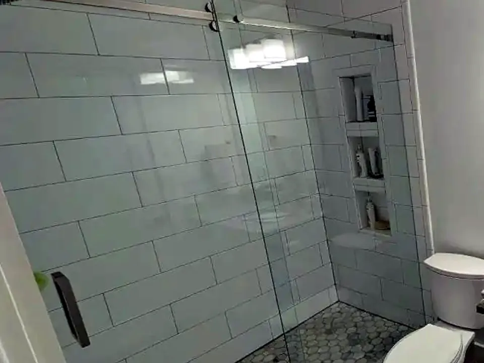 Shower with a sliding glass door, large white wall tile and a built-in niche