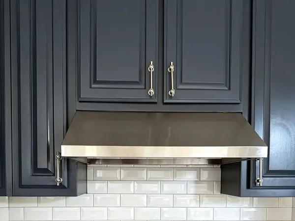 White subway tile backsplash under a stainless range hood between navy cabinets